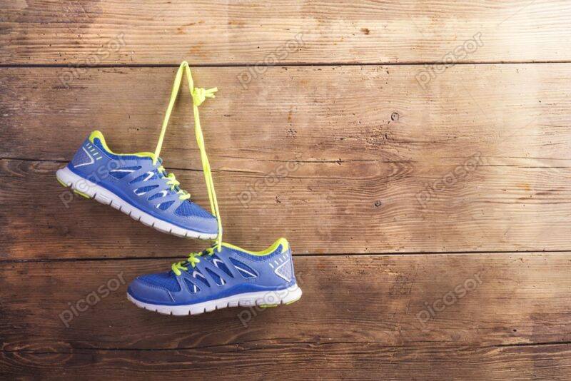عکس کفشهای ورزشی آویزان از بند روی دیوار چوبی